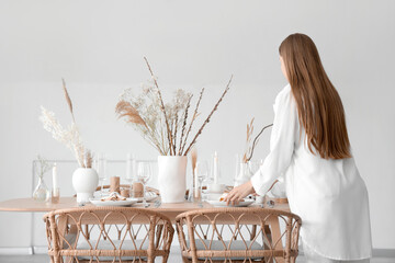 Beautiful woman setting table with dried flowers in dining room - obrazy, fototapety, plakaty