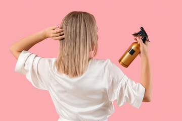 Young blonde woman with hair spray on pink background, back view