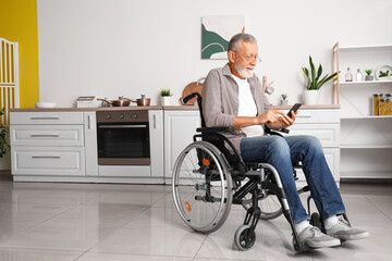 Senior man in wheelchair using mobile phone at home - obrazy, fototapety, plakaty