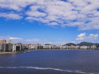 View of Icaraí Beach in Niterói, Rio de Janeiro, Brazil, tall buildings, calm waters of Guanabara Bay and blue sky with clouds on a spring afternoon