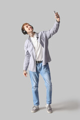 Happy young man in headphones taking selfie on grey background