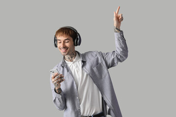 Happy young man listening to music with headphones and mobile phone on grey background