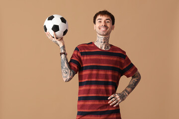 Happy young man with soccer ball on brown background