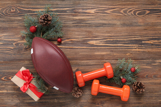 Composition with dumbbells, rugby ball, gift box and Christmas tree branches on wooden background