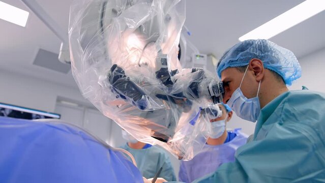 Doctors look at microscope covered in plastic during surgery. Modern neurological operation in hospital. Low angle view.