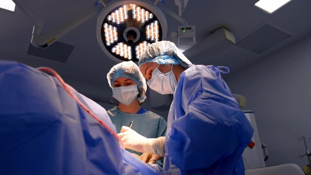 Two female medics working in surgery room. Surgeon uses metal instruments performing operation. Low angle view.