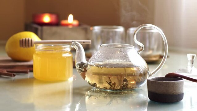 Teapot with hot steamed green tea on table with caps, honey and lemon. 4K Video