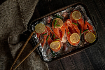 Raw fish trout steak on board on black background with lemon and spices