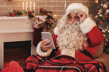 Santa Claus with tablet computer at home on Christmas eve