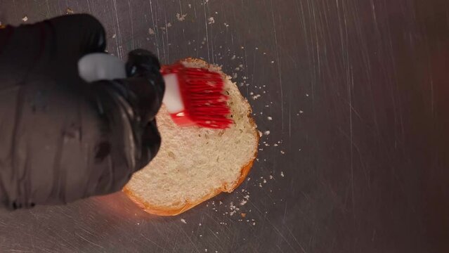 Chef in black gloves making burge. spread sauce on bun. Close-up of a skilled craftsman working at the workplace 