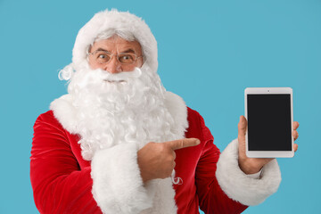 Santa Claus pointing at tablet computer on blue background
