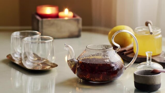 Teapot with hot steamed black tea on table with caps, honey and lemon. 4K video