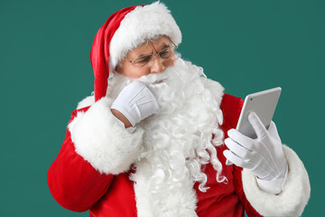 Thoughtful Santa Claus with tablet computer on green background