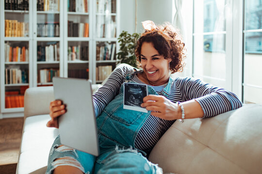 Pregnant woman resting on couch and holding her child ultrasound picture