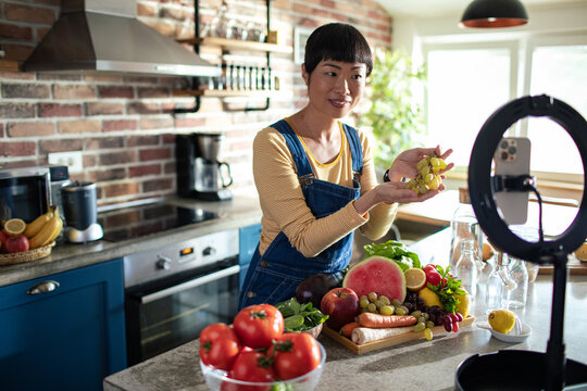 Female nutritionist giving advice about vegetables to her followers on a smartphone in the kitchen