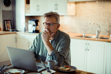 Middle aged man using laptop on kitchen table