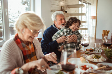 Loving grandfather embracing his joyful grandson during a family meal