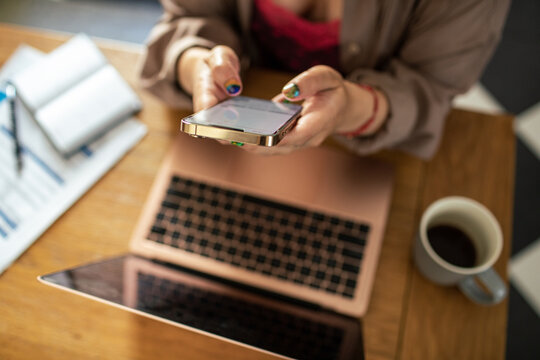 Top view of woman texting on smartphone with laptop on desk