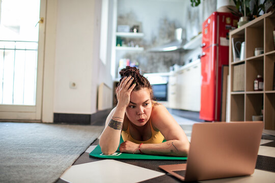 Tired woman on yoga mat looking at laptop
