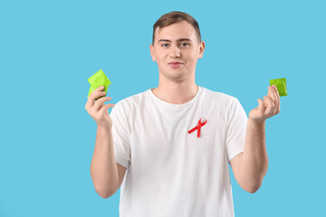 Handsome young man with red ribbon and condoms on blue background. World AIDS day concept