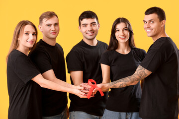 Group of young people with red ribbons on yellow background. World AIDS day concept