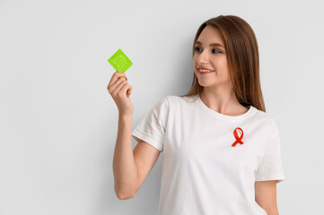 Pretty young woman with red ribbon and condom on white background. World AIDS day concept