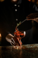 Female bartender hands hold a green leaf with tweezers over a glass with a cocktail