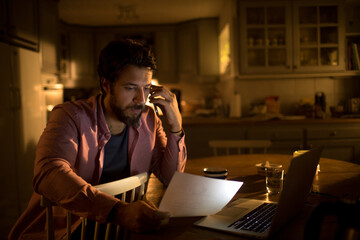Stressed man holding document making phone call at home