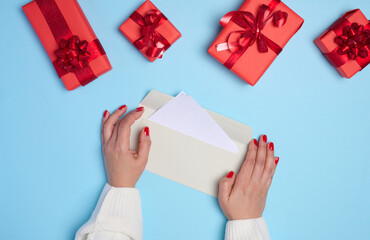 Female hands holding a white paper envelope on a blue background, around a box with gifts