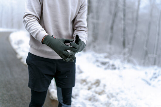 Picture of a man's hands, wearing gloves and sports clothes.Warm up before going on a run in the foods on a snowy winter day, trees and ground are cover in snow