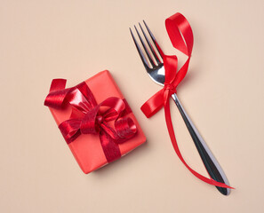 Gift box and fork on beige background, top view
