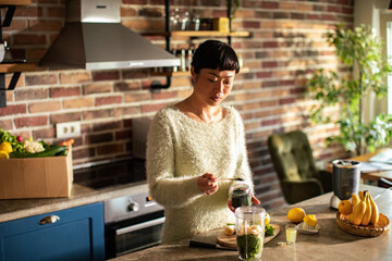 Woman is preparing a healthy detox drink in a blender in kitchen - obrazy, fototapety, plakaty