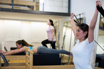Fototapeta na wymiar Young Hispanic woman performing set of pilates exercises on reformer in modern fitness studio