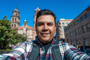 Latino taking a selfie in a mexican colonial town downtown with a cathedral on the background
