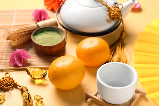 Teapot with mandarins, bowl of powdered matcha tea, chasen and oriental symbols on yellow background. New Year celebration