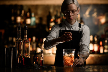 Female bartender mixes a cocktail with ice in a mixing glass with a long bar spoon