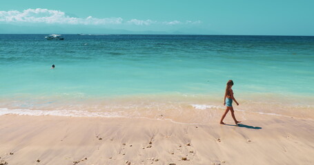Young woman taking a peaceful stroll along a serene tropical beach. Girl walking white sand,...