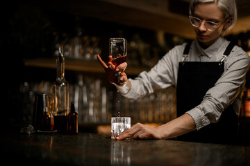 Female bartender skillfully holds a small geyser bottle and pours a drink from it into a glass with...