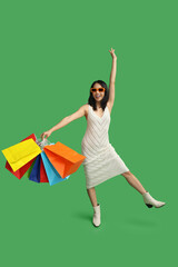 Young Asian woman in sunglasses with shopping bags on green background