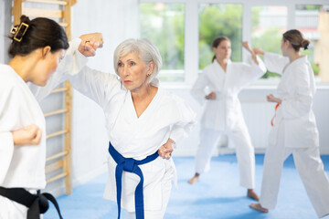 Women in white kimonos are engaged in wrestling at sports training. Woman paired up with female partner performs classic techniques of repelling blow in karate technique
