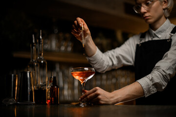 Female bartender adds a few drops of drink to a ready-made cocktail in a cocktail glass with a pipette