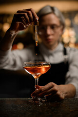 Female bartender adds a drink drop by drop to a cocktail glass with a dropper