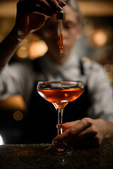 Female bartender adds a drink drop by drop to a cocktail glass with a dropper on a blurred background