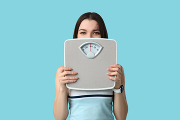 Beautiful young sporty woman with scales on blue background. Weight loss concept