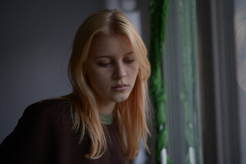 portrait of a girl 18 years old with blond hair near the window on a rainy day