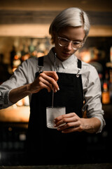 Female bartender stirs something in a frosted glass with a long bar spoon