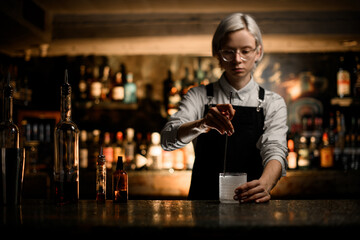 Woman bartender stirs something in a frosted glass with a long bar spoon