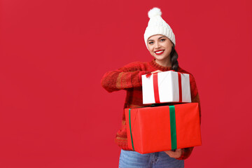 Beautiful young woman with Christmas gifts on red background