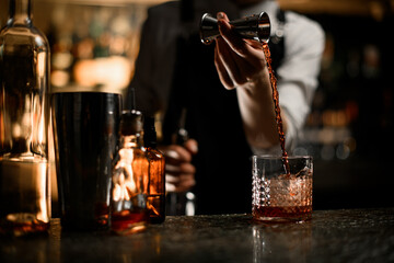 Female hands pour an alcoholic drink from jigger into a glass