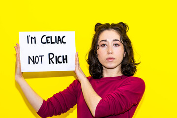 Young Latina woman holding a sign that reads IM CELIAC, NOT RICH. Economic difficulties for celiac people shopping.